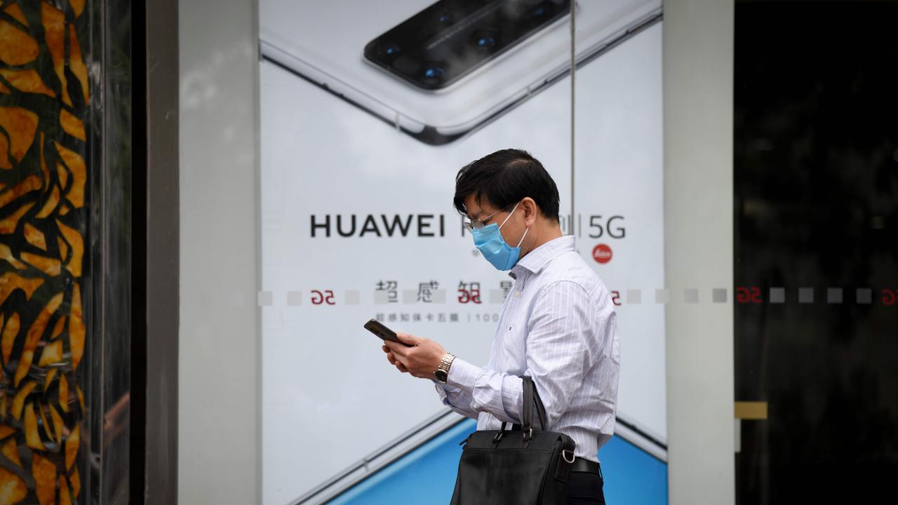 A man uses his mobile phone as he walks past a poster of Huawei P40 in Beijing (Photo by WANG Zhao / AFP)