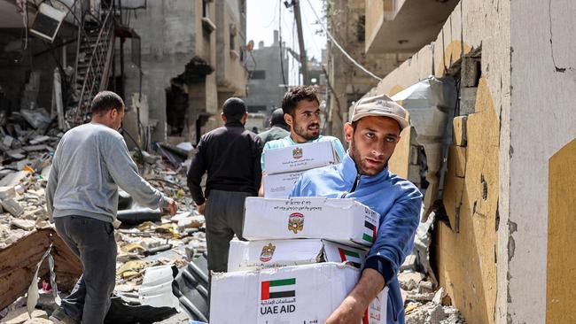 Men walk through rubble past damaged buildings with aid packages collected from a drop over the northern Gaza Strip. Picture: AFP