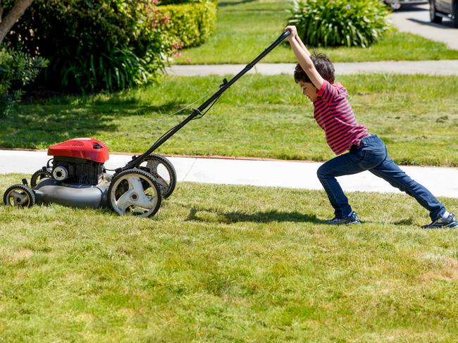 Stock photo of a small boy attempting to mow a lawn in a suburban neighborhood . iStock.