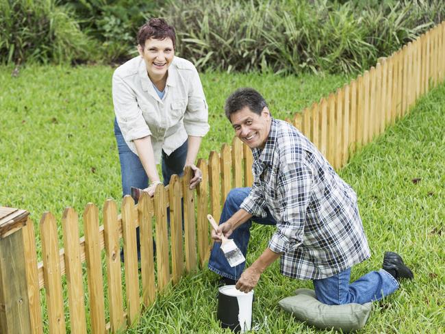 Mature couple (50s, Hispanic / Native American) standing in back yard, painting fence.