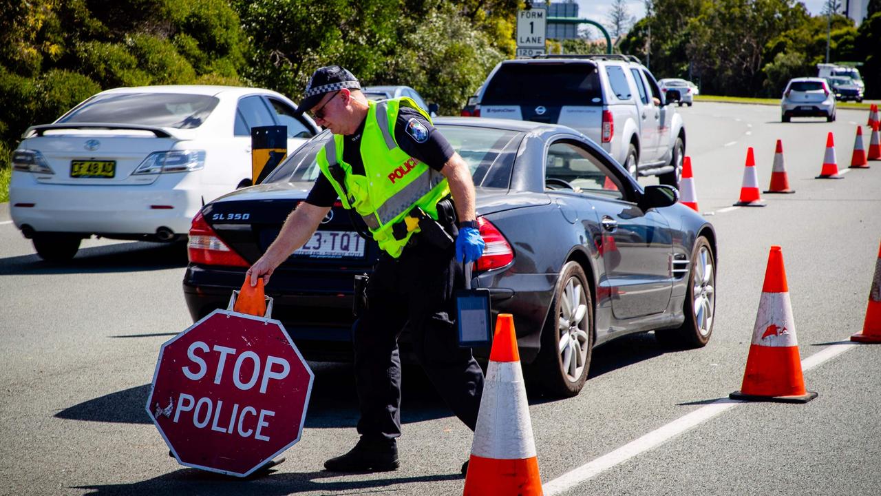 A Queensland police officer moves a stop sign at a vehicle checkpoint on the Pacific Highway on the Queensland - New South Wales border. Photo: Patrick Hamilton / AFP