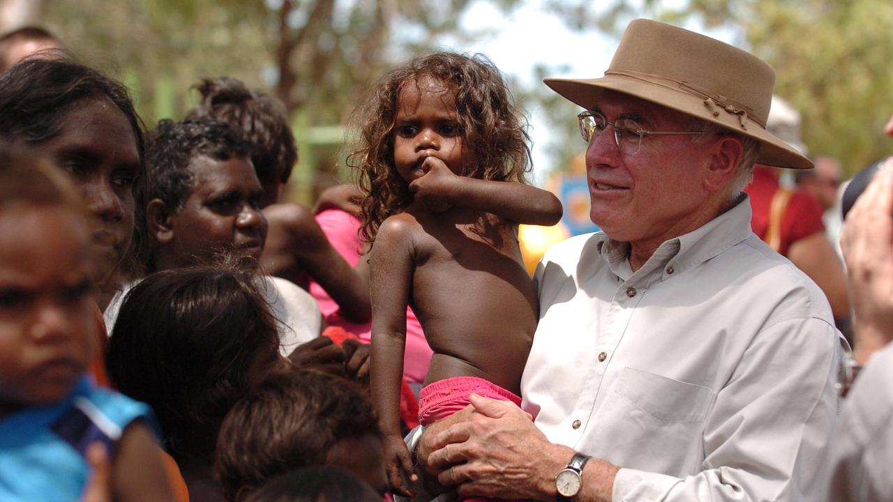 Mr Howard holds young girl and speaks to locals during a tour of the NT Aboriginal community of Wadeye, south west of Darwin.