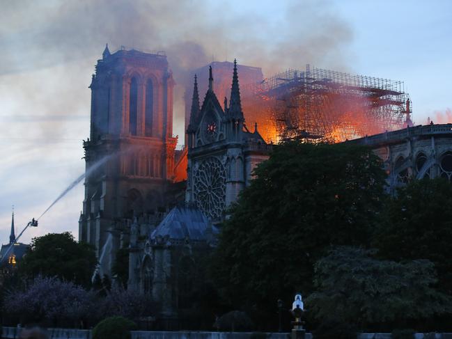 A firefighter tackles the blaze as flames and smoke rise from Notre Dame cathedral as it burns in Paris, Monday, April 15, 2019. Massive plumes of yellow brown smoke is filling the air above Notre Dame Cathedral and ash is falling on tourists and others around the island that marks the center of Paris. (AP Photo/Michel Euler)