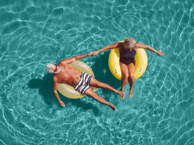 High angle view photo of a senior couple floating in the ocean while using swimming and floating devices; active retirement travel generic