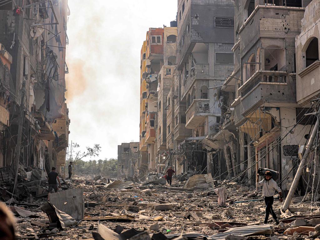 A man carries a propane gas cylinder on his back while walking through debris and destruction littering a street in the Jabalia camp for Palestinian refugees in Gaza City.