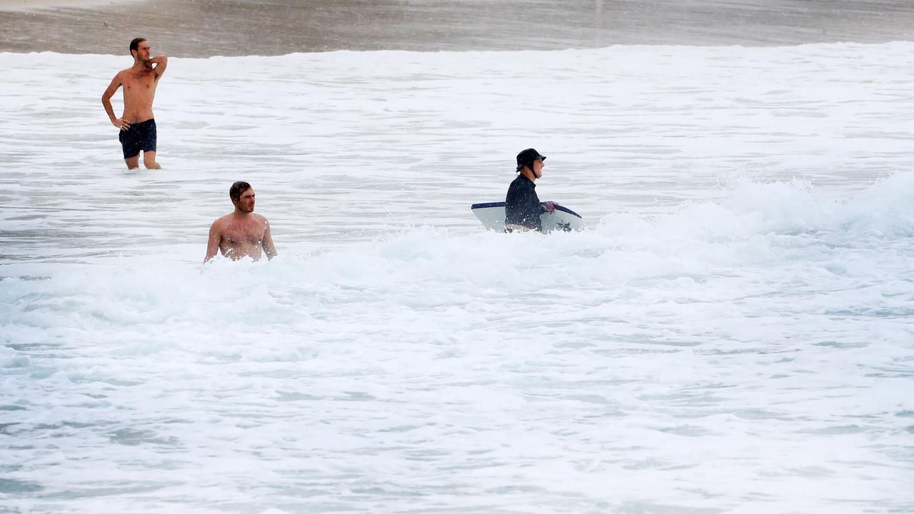 An almost empty beach at Burleigh Beach as three swimmers brave the rain as wet weather descended over the Gold Coast. Photo: Scott PowickNEWSCORP