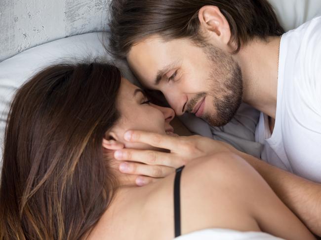 Happy affectionate young couple lying in bed face to face, smiling lovers enjoying intimacy and pleasant morning together, man tenderly touching woman, love and sensuality concept, close up top view