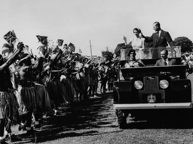 Queen Elizabeth II and Prince Philip wave to a group holding up Union Jack Flags, as the royal couple stand in the back of the Royal Land Rover in Townsville, Australia in March 1954. Picture: Paul Popper/Popperfoto/Getty Images