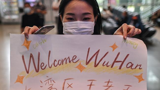 A woman wearing a face mask displays a welcome sign for a passenger at Tianhe Airport in Wuhan on September 24. Picture: Hector Retamal/AFP