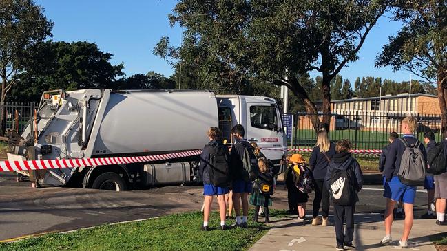 Schoolchildren stop to look at the garbage truck in the sinkhole in Namona St, Narrabeen. Picture: Jim O'Rourke.