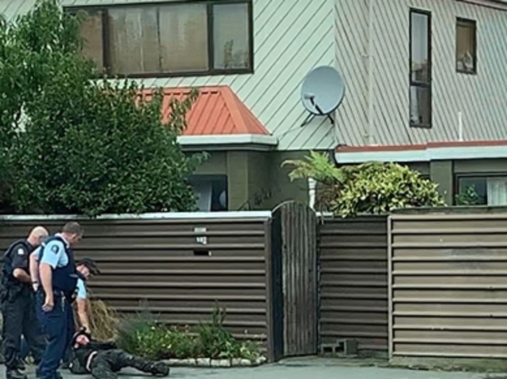 Two police officers arresting the gunman after dragging him out of his Subaru and onto a footpath.