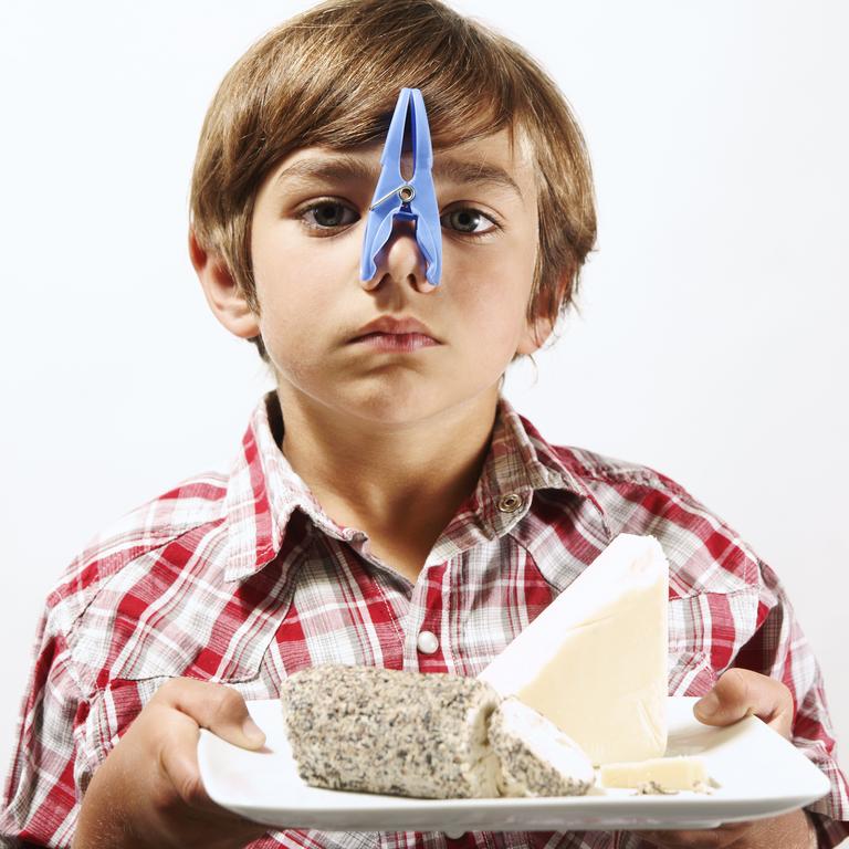 A boy with a clothes peg on his nose holding a plate of stinky cheese.