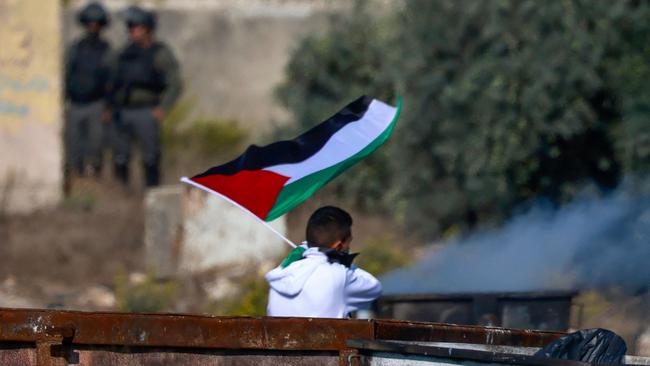 A Palestinian youth waves the national flag amid clashes with Israeli forces at the northern entrance of Ramallah.