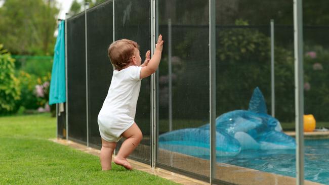 Baby leaning on swimming pool fence protection.