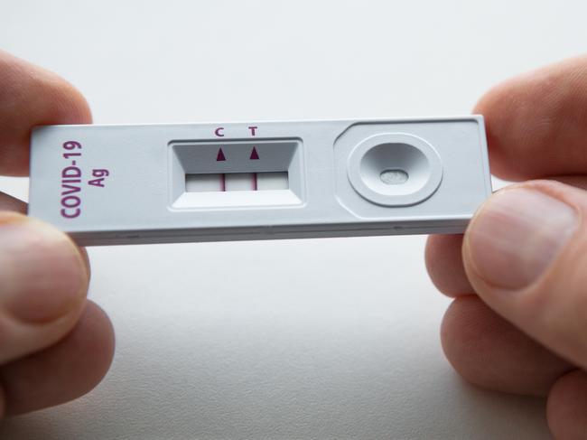 Rapid antigen detection test (RADT) with two red stripes showing a POSITIVE result of a human sample testing. Mans fingers holding the white plastic device with a COVID-19 Ag inscription.