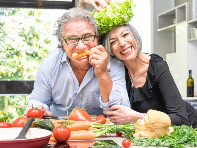 Senior couple having fun in kitchen with healthy food - Retired people cooking meal at home with man and woman preparing lunch with bio vegetables - Happy elderly concept with mature funny pensioner