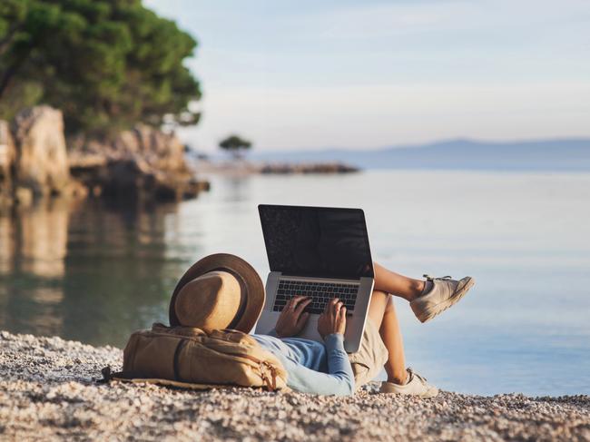 Young woman using laptop on a beach. People using devices to plan trips, check in to hotels and flights, stay connected to family and office. Picture: iStock