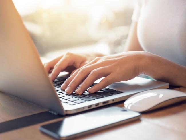 Closeup woman's hands typing on a laptop that is on a wooden desk with a mobile smartphone and mouse computer