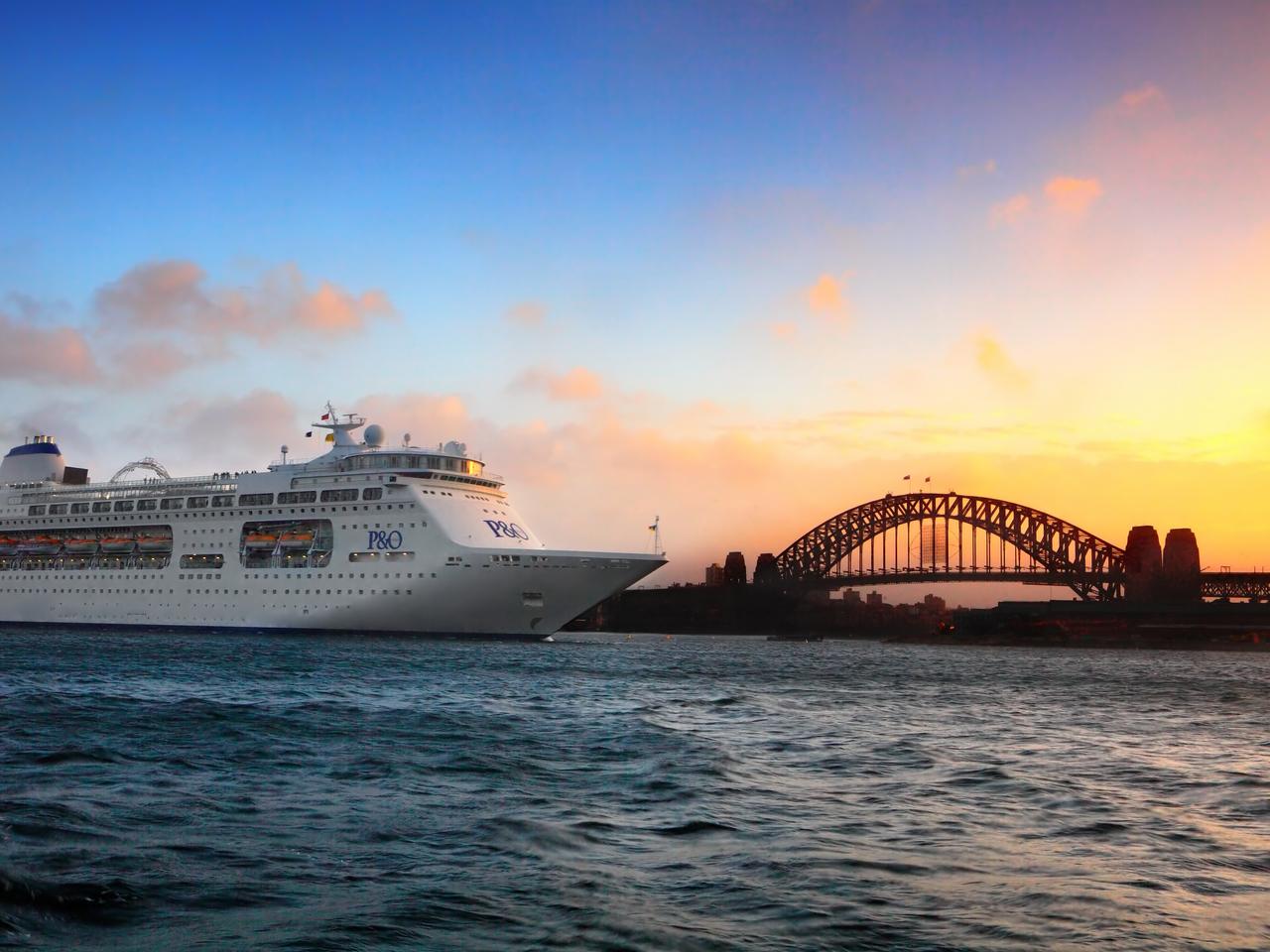 Sydney, Australia - December 29, 2013; P & O cruise ship navigates choppy harbour waters at sunrise by a silhouetted view of Sydney Harbour Bridge