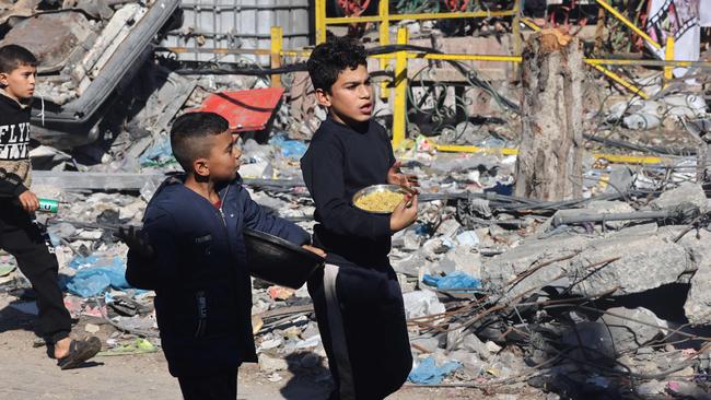 Palestinian children carry donated food past the rubble of buildings destroyed in Israeli army strikes in the southern Gaza Strip city of Rafah during the truce on November 30. Picture: Mohammed Abed/AFP