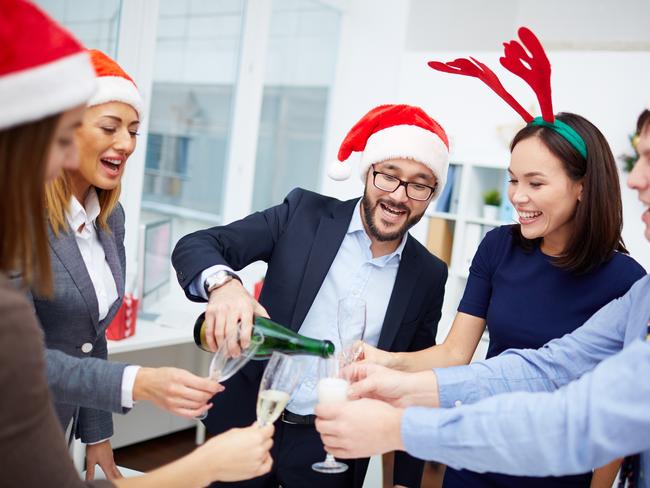 Happy businessman in Santa cap pouring champagne into flutes of his colleagues in office