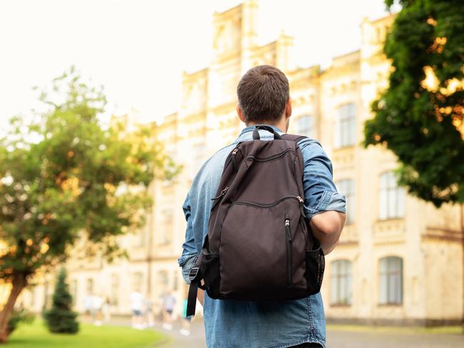 Student university standing with his back to the camera and his backpack on one shoulder and walking in university campus, education concept. Young man walking down street with a backpack. Back view.