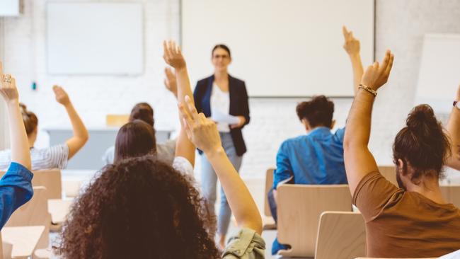 Male and female students raising hands in classroom. Men and women are answering to mature teacher. They are together in university.School roomclassroomgenericschool