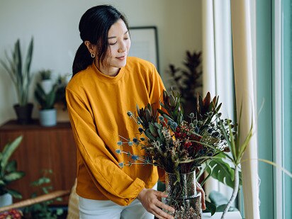 Young Asian woman receiving bouquet of flower delivery at home. Arranging flowers in a vase and decorating in the living room at home