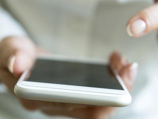 Young caucasian in white shirt and green jeans holding her white smart phone and typing or browsing thru the apps. Image is taken with Nikon D800 and 24-70/2.8 lens from close distance, shallow depth of field, focus on smart phone. Smart phone is not recognizable.