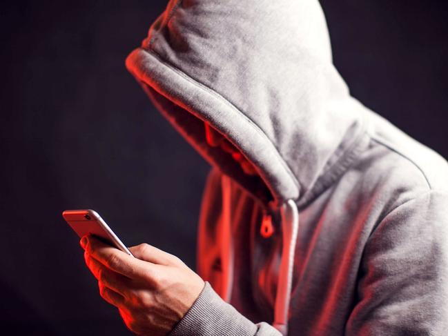 Man wearing hoody sweater with mobile phone in hands. Crime and hacking concept; scam generic.