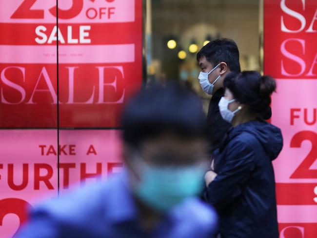 People wearing face masks as a preventative measure against coronavirus COVID-19 walk in front of sales signs in Sydney, Sunday, March 15, 2020. Prime Minister Scott Morrison has warned all Australians they could face more changes to their day-to-day lives to try curb the spread of COVID-19. (AAP Image/Steven Saphore) NO ARCHIVING