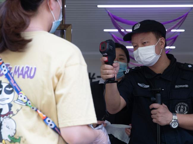 A security guard checks the body temperature of a woman in Wuhan. Picture: AFP.