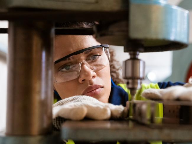 TRADESWOMAN/ TRADE WOMAN/ TRADESMAN/ TRADIE/BUILDING INDUSTRY: Close-up of female apprentice using yoke machine. Female engineer is wearing protective glasses in factory. She is working in manufacturing industry.