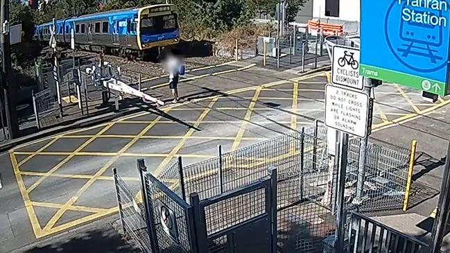 A pedestrian walks into a level-crossing as a train approaches Prahran station early in 20222