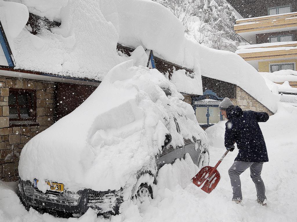 A ski tourist removes snow from a car after heavy snowfalls in Austria, that grounded planes and threw travel into chaos. Picture: AP Photo/Matthias Schrader