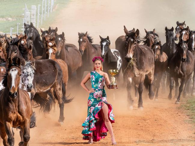 Melbourne Cup Carnival Ambassador Olivia Molly Rogers stands in front of galloping horses with the 2018 Lexus Melbourne Cup at Bogong Horseback Adventures station in Tawonga. Picture: Jason Edwards