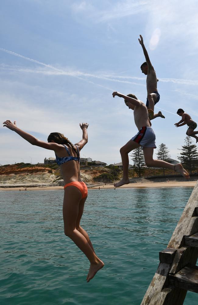 Teenagers leap into the water from the Port Noarlunga jetty. Picture: AAP / David Mariuz