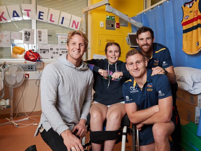 Katelin Gunn, 15, flanked by Adelaide players Rory Sloane, Rory Laird and Andy Otten in her room at the Women's and Children's Hospital. Thanks to Variety, Katelin will be at the top of the race on Saturday when the Crows run on to Adelaide Oval for Showdown 46. Picture: Matt Loxton