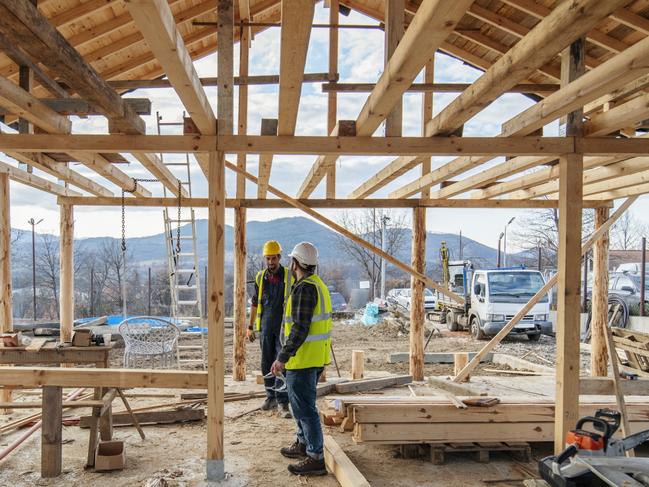 Construction workers in building site of wooden house.