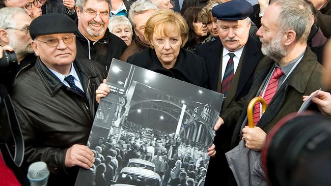 Former Russian President Mikhail Gorbachev (L), German Chancellor Angela Merkel (C) and former Polish President Lech Walesa hold a signed print of people crossing the Boesbrucke border bridge during a ceremony to mark the 20th anniversary of the fall of the Berlin wall. Picture: Getty Images.