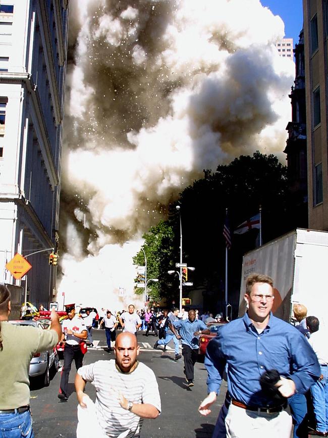 Pedestrians run from the scene as one of the World Trade Center Towers collapses in New York City.