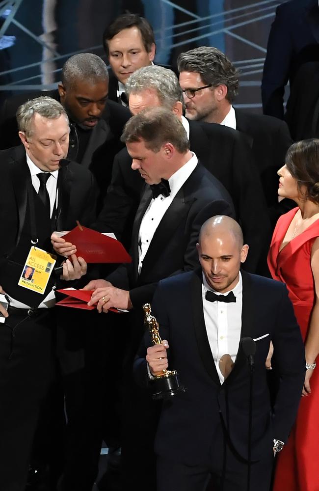 La La Land producer Fred Berger speaks at the microphone as production staff and representatives from PricewaterhouseCoopers, Martha L. Ruiz and Brian Cullinan, consult behind him regarding a presentation error of the Best Picture award. Picture: Getty