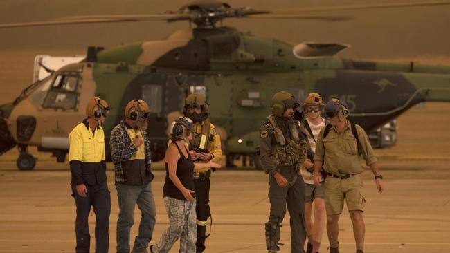 Members of the Tytherleign family are escorted from the HMAS Albatross 808 Squadron Flight line by Leading Seaman Aircrewman Ben Nixon and Rural Fire Service employee Dwyane Graham after being evacuated from their property near the Tianjara bushfire.