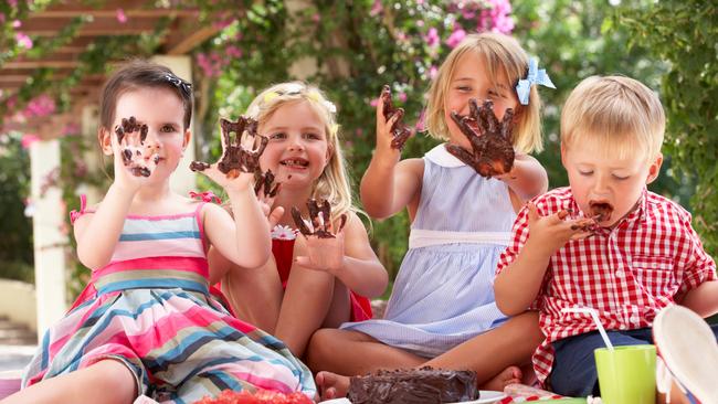 Group Of Children Eating Jelly And Cake At Outdoor Tea Party Raising Hands Covered In Chocolate Happy