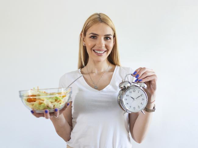 Young woman holding clock and Healthy food of salad Intermittent fasting concept. Time to lose weight , eating control or time to diet concept.