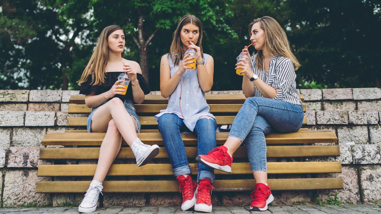 Group of teenage girls sitting on a bench and drinking orange juice.