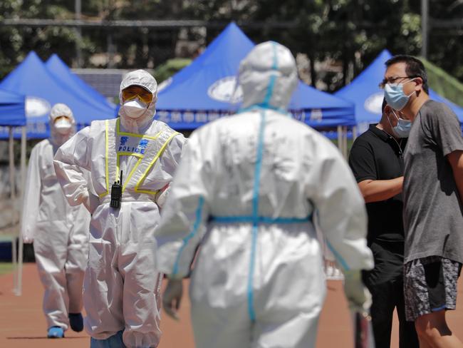 A policeman wearing a protective suit stands watch people living surrounding the Xinfadi wholesale market arrive to get a nucleic acid test at a stadium in Beijing, Sunday, June 14, 2020. China is reporting its highest daily total of coronavirus cases in two months after the capital's biggest wholesale food market was shut down following a resurgence in local infections. (AP Photo/Andy Wong)