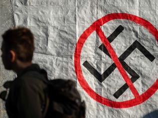 A man walks next to a logo of Nazi swastika during an anti-fascist rally outside the Court of Appeal during the testify of former MP and leader of Golden Dawn party Nikolaos Michaloliakos, on November 6, 2019, in Athens. - The 61-year-old Holocaust denier is one of nearly 70 defendants facing sentences of five to 20 years in prison. The main charge against them is participation in a criminal organisation, in addition to a host of other indictments related to murder and assault. (Photo by Angelos Tzortzinis / AFP)