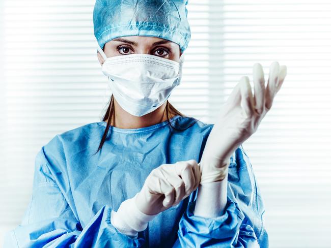 Portrait of Female doctor Surgeon in blue scrubs putting on surgical gloves and Looking at Camera