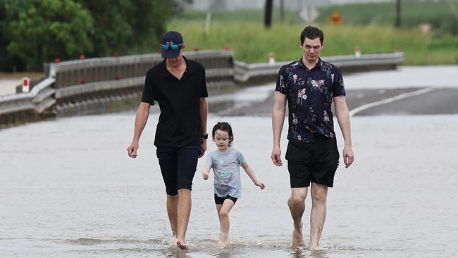 A monsoonal tropical low pressure system has brought devastating widespread flooding to North Queensland. Robin Watson, Ella Watson, 5, and her father Leal Watson walk along the Bruce Highway after the road was cut off by flood water south of the Tully River at Euramo. Picture: Brendan Radke